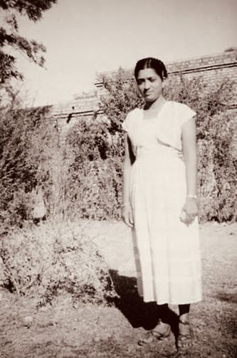 A young woman in a pale sari standing on open ground in India.